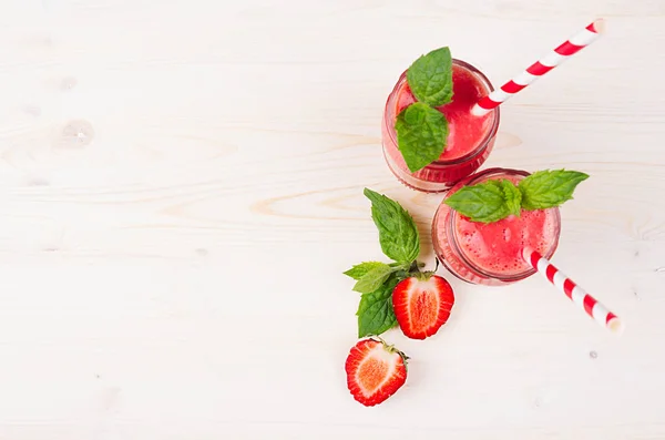 Smoothie de morango vermelho recém-misturado em frascos de vidro com palha, folha de hortelã, amadurecimento de corte, vista superior. Branco placa de madeira fundo, espaço de cópia . — Fotografia de Stock