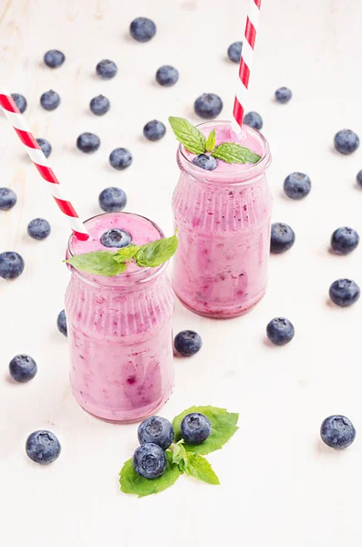 Batido de fruta de arándano violeta recién mezclado en frascos de vidrio con paja, hojas de menta, bayas. Fondo tablero de madera blanco . —  Fotos de Stock