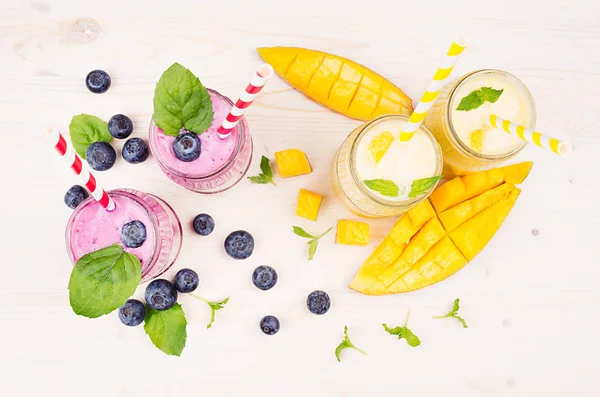 Freshly blended yellow and violet  fruit smoothie in glass jars with straw, mint leaves, mango slices, berry, top view.