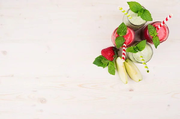 Čerstvé zelené a červené ovocné lichotníku jahody a jablka ve skleněných nádobách se slámou, lístečky máty, pohled shora. — Stock fotografie