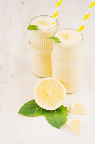 Frullato di limone giallo appena miscelato in vasi di vetro con paglia, foglia di menta, limone tagliato, primo piano . — Foto Stock