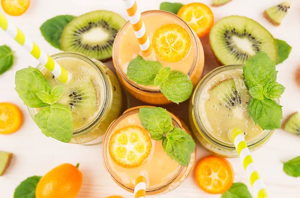 Čerstvě směsových oranžová kumquat a ovocné smoothie ve skleněných nádobách se slámou, list máty, zelené kiwi řez zralé bobule, pohled shora, zblízka. — Stock fotografie