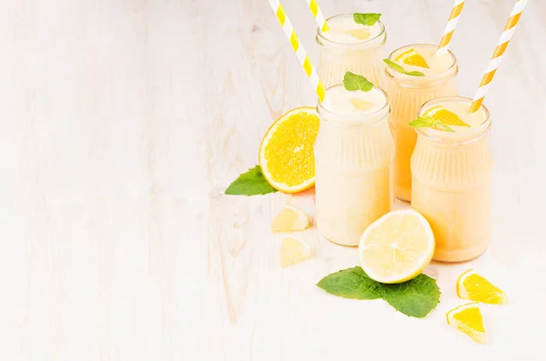 Batido de limón amarillo y naranja recién mezclado en frascos de vidrio con paja, hoja de menta, espacio para copiar . — Foto de Stock