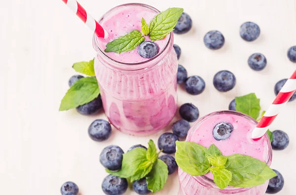 Batido de fruta de arándano violeta recién mezclado en frascos de vidrio con paja, hojas de menta, bayas. Fondo de tablero de madera blanco, espacio de copia . —  Fotos de Stock