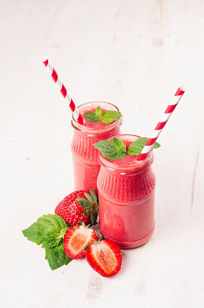 Batido de fruta de fresa roja en frascos de vidrio con paja, hoja de menta, bayas maduras cortadas. Fondo de tablero de madera blanco, espacio de copia . —  Fotos de Stock