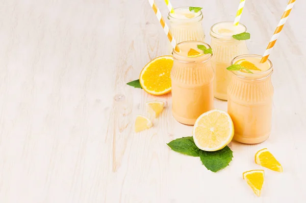 Batido de limón amarillo y naranja recién mezclado en frascos de vidrio con paja, hoja de menta, espacio para copiar. Fondo tablero de madera blanco . —  Fotos de Stock