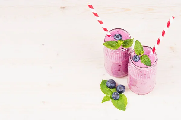 Batido de fruta de arándano violeta recién mezclado en frascos de vidrio con paja, hojas de menta, bayas. Fondo de tablero de madera blanco, espacio de copia . —  Fotos de Stock