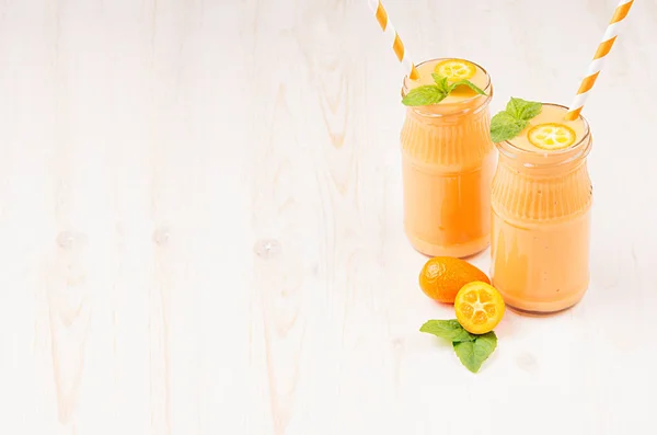 Freshly blended orange citrus kumquat  fruit smoothie in glass jars with straw, mint leaf, cute ripe berry, copy space. White wooden board background. — Stock Photo, Image