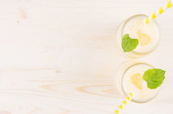 Frullato di limone giallo appena miscelato in vasi di vetro con paglia, foglia di menta, vista dall'alto. Fondo bordo di legno bianco, spazio copia . — Foto Stock