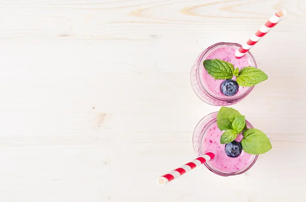 Batido de frutas de arándano violeta recién mezclado en frascos de vidrio con paja, hojas de menta, vista superior. Fondo de tablero de madera blanco, espacio de copia . —  Fotos de Stock