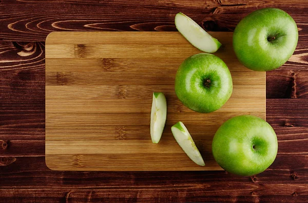 Manzanas verdes con rodajas y tabla de cortar de bambú en tablón marrón, vista superior, espacio para copiar . — Foto de Stock