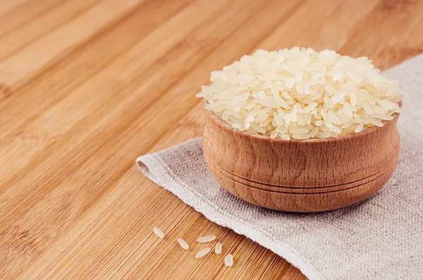 Arroz blanco basmati en cuenco de madera sobre tabla de bambú marrón, primer plano. Estilo rústico, cereales dietéticos saludables fondo . — Foto de Stock