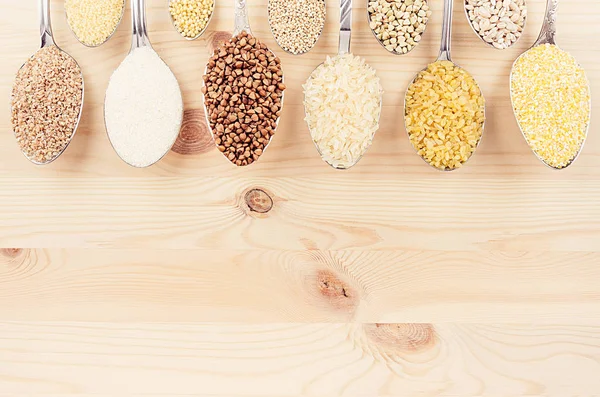 Grano de cereales diferentes en cucharas sobre tabla de madera beige como fondo decorativo. Vista superior . — Foto de Stock