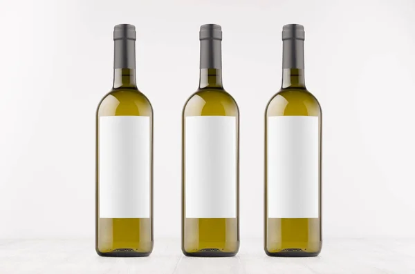Tres botellas de vino verde con etiquetas blancas en blanco en tablero de madera blanco, se burlan de . — Foto de Stock