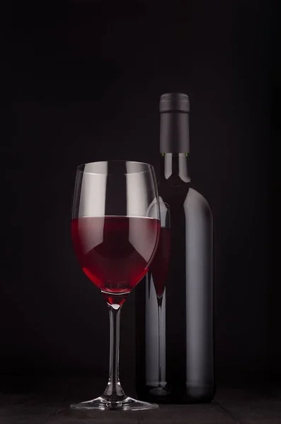 Botella de vino tinto y copa de vino se burlan de fondo de madera negro oscuro elegante, vertical . — Foto de Stock