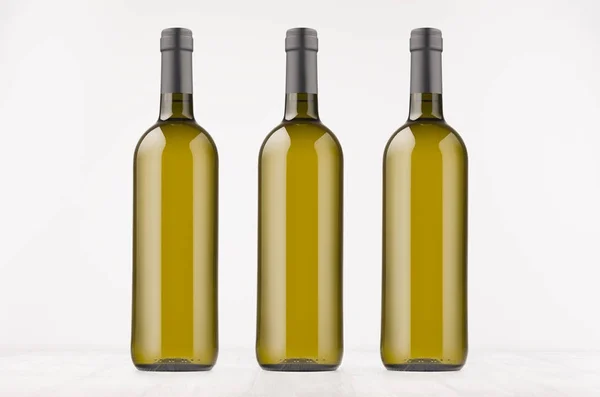 Tres botellas de vino verde con vino blanco sobre tabla de madera blanca, simulan . — Foto de Stock