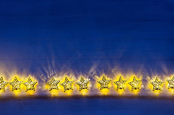 Weihnachtsbeleuchtung gelbe Sterne brennen auf dunklem ultramarinem Holzhintergrund. — Stockfoto