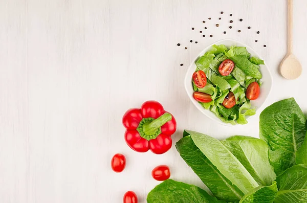 Fresh salad of green leaves, red cherry tomatoes, paprika on white wood board, top view.