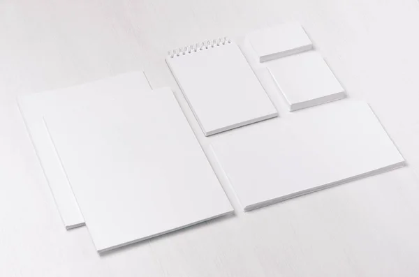 White blank business card, envelope, brochure, notepad, stickers on soft white wood board, inclined.