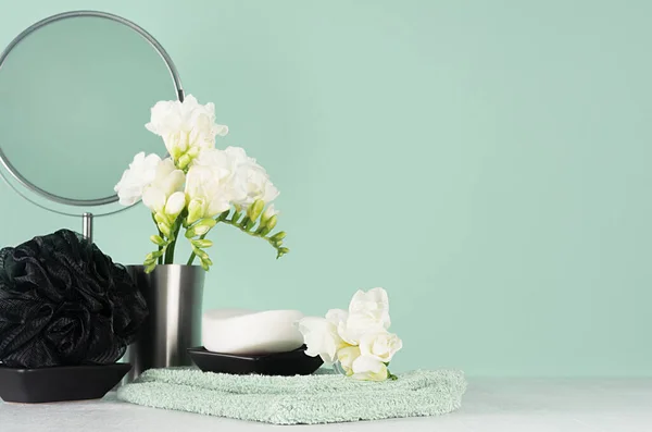 Fashion toiletry accessories in black and silver color in green mint menthe and white interior - mirror, towel, soap, bath puff, spring fresh flowers, closeup.