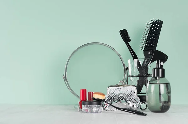 Dressing table with black cosmetics and accessories on green mint menthe wall and white table - mirror, comb, red nail polish, cosmetics bag, spray bottle.