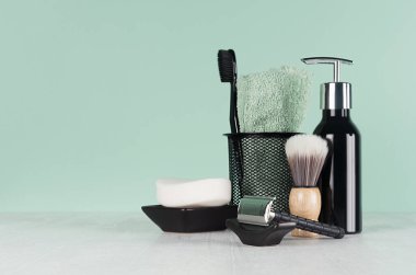 Stylish bathroom interior with black shaving accessories on green  wall, white table - razor, toothbrush, towel, soap, shave brush, dispenser.