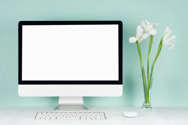 Spring home office for business with blank pc, keyboard, mouse and white fresh flowers in glass vase in light green mint menthe interior on white wood desk.