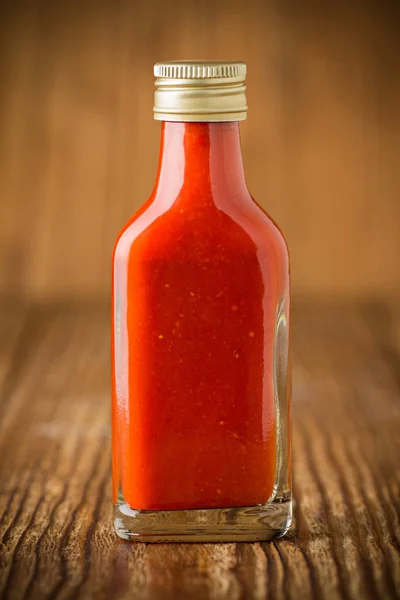 Hot chili szósz, üvegből, fából készült háttér — Stock Fotó