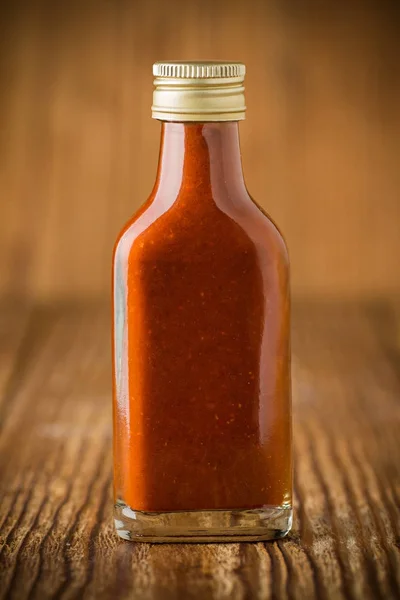 Hot chili sauce in glass on wooden background — Stock Photo, Image