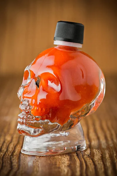 Salsa picante de chile en un vaso en forma de calavera sobre fondo de madera — Foto de Stock