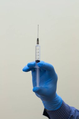 Doktorun elinde şırıngayla gri arka planda iğne tutuşu görüntüsü