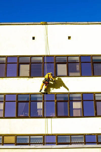 男はファサードを修復し窓を洗浄する建物の高高度作業を行います — ストック写真