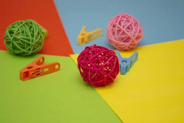 colored rattan balls on colored paper with colored paper clips. green ball pink and red.