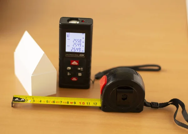 Masa arkaplanı, uzunluk ölçme aleti, lazer metre, cetvel, masanın üzerindeki beyaz ev modeli.