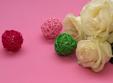 Pembe arka planda taze beyaz gül. Yakınlarda üç tane turta topu var. Yeşil, kırmızı pembe. Metin için boşluk