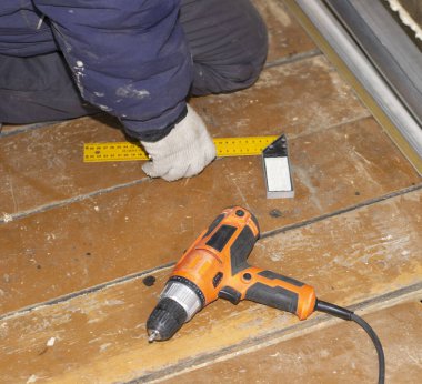 Mavi ceketli bir işçi inşaat alanındaki bir odun parçasıyla ölçüm yapıyor. Ahşap bir evde onarım. Yakınlarda bir tornavida var.