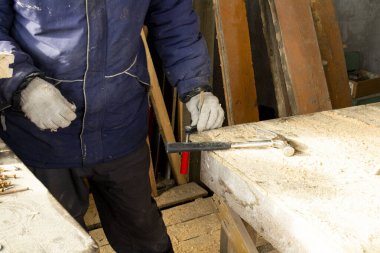 Mavi ceketli bir işçi ahşap masadaki kıskacı tamir ediyor. Ahşap bir evde onarım
