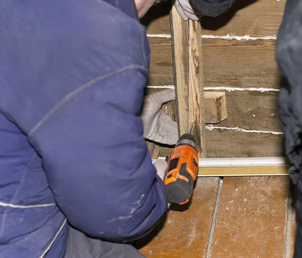 the worker fastens the wooden rail with an electric screwdriver to the wall. repair in a wooden house