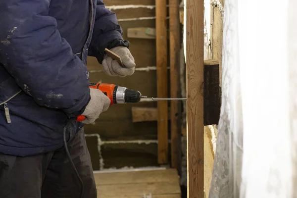 the worker fastens the wooden rail with an electric screwdriver to the wall. repair in a wooden house