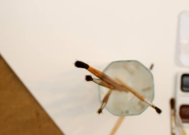 Boya için fırçalı cam ve beyaz bir kağıt. Çuval bezi kahverengi arkaplan, düz yatış, metin için boşluk.