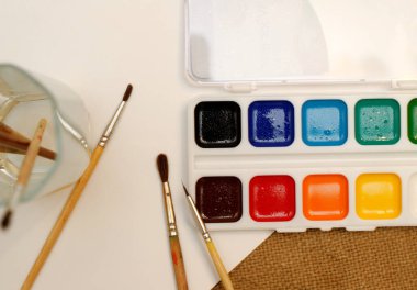 Fırçalı yeni suluboya resimler ve beyaz bir kağıt. Çuval bezi kahverengi arkaplan, düz yatış, metin için boşluk.