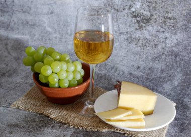 Tabakta bir bardak beyaz şarap peyniri ve bir demet üzüm kompozisyonu. Çuval bezli gri bir arkaplan. yakın plan.