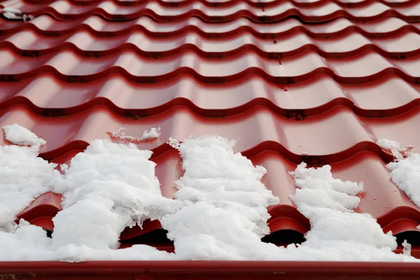 the remains of snow on the roof of the house from metal roof tiles. spring has begun snow is melting