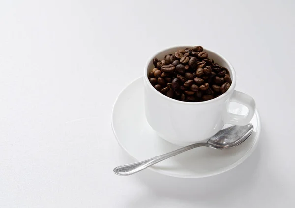 Grãos Café Uma Xícara Branca Com Prato Colher Fundo Branco — Fotografia de Stock