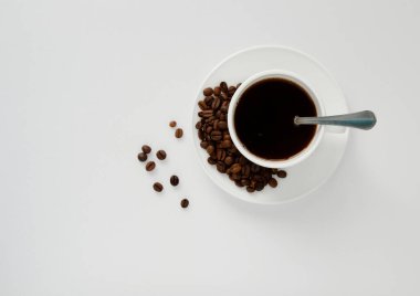 Kahve fincanı, fincan tabağında kahve çekirdekleri ve beyaz bir masanın üzerinde. Düz yat. en üstteki görünüm.