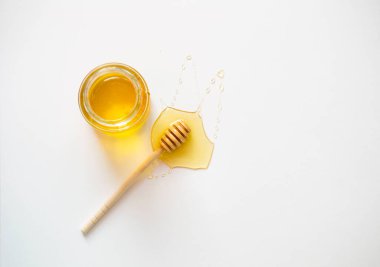 Ballı cam kavanoz ve beyaz arka planda tahta bir bal çubuğu..