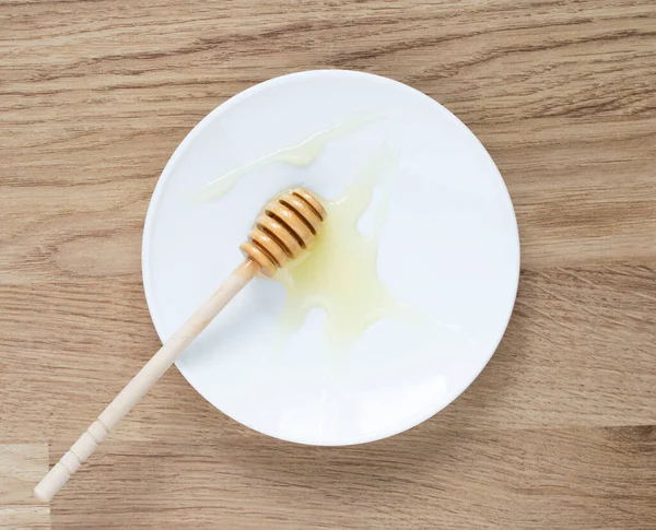 Houten stokje honing op een witte schotel. honing druipend van honingstok. — Stockfoto