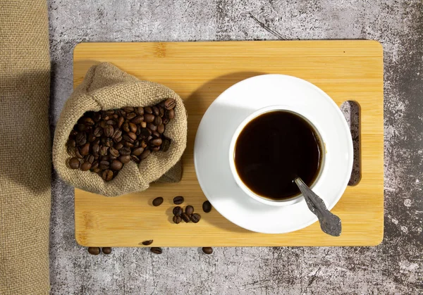 Granos de café en una bolsa y una taza blanca con café. bandeja de madera . —  Fotos de Stock