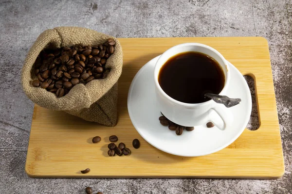 coffee beans in a bag and a white cup with coffee. wooden tray.