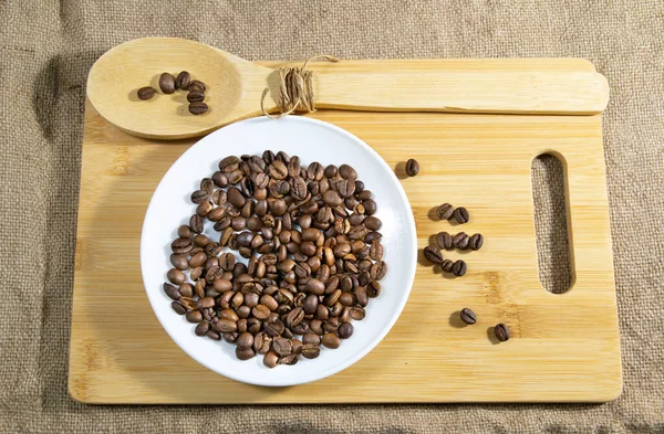 coffee beans in white saucer with a wooden spoon. sackcloth background.